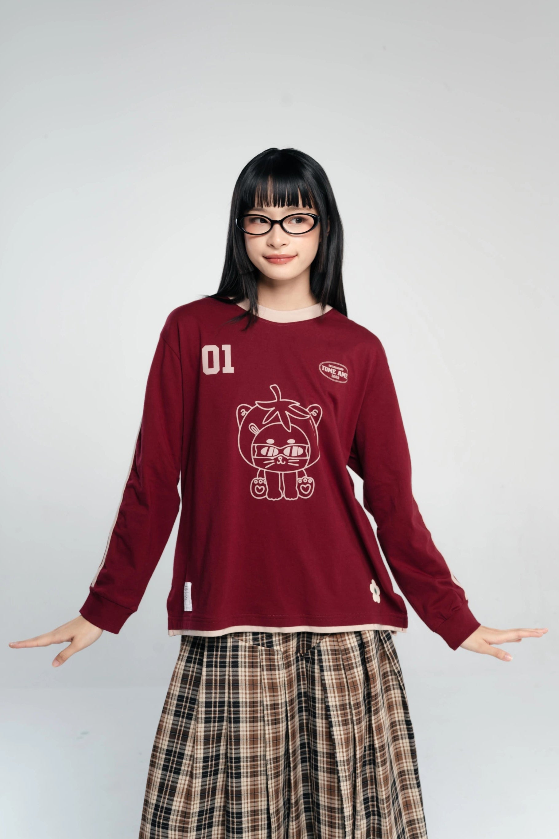 Person wearing a maroon long-sleeve tees with a graphic design by Tome Ame on a plain background