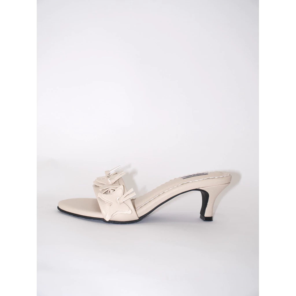Broken white high-heeled sandal by Takkan Shoes with a decorative bow on a white background
