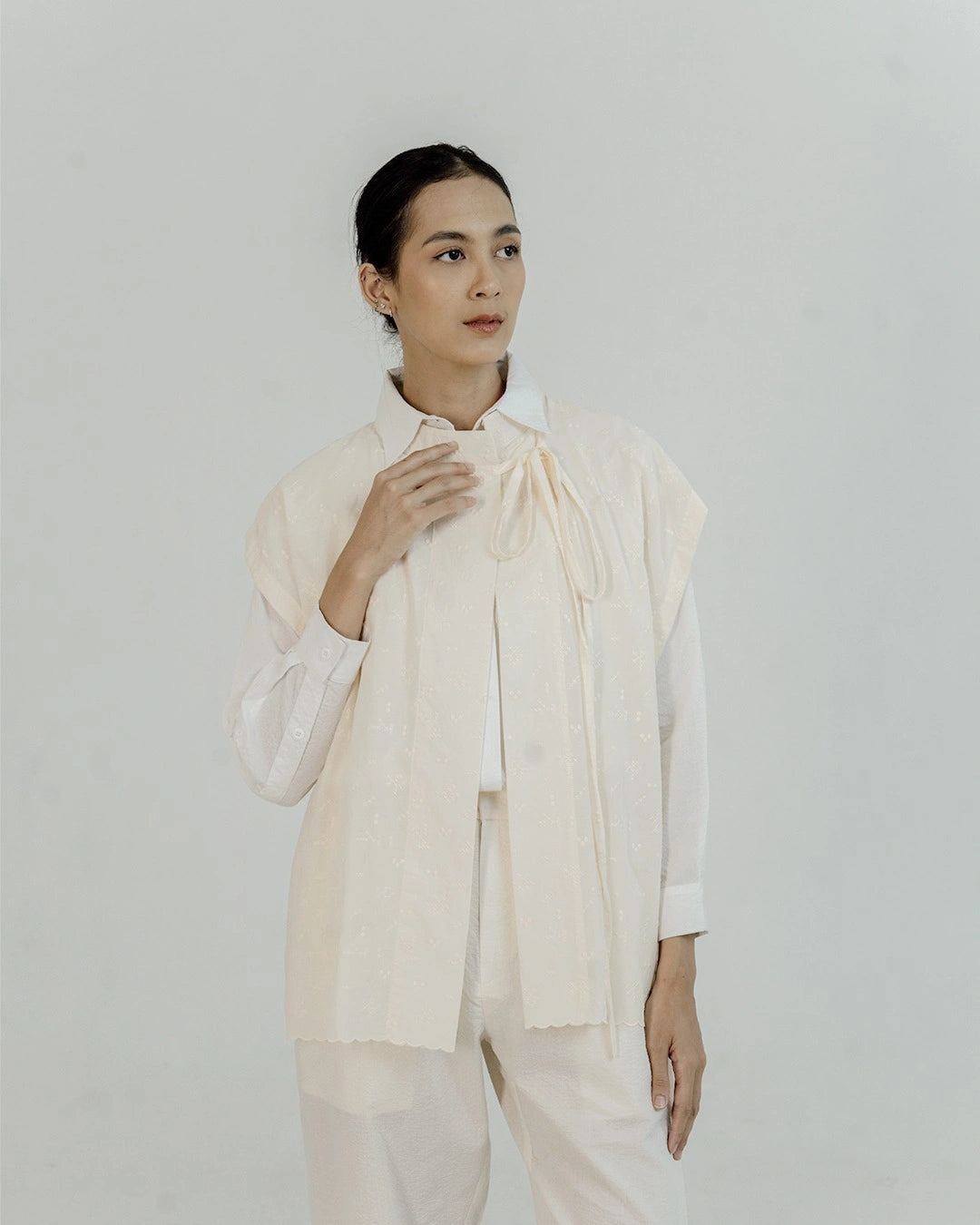 Person wearing a broken white sleeveless outer by Damakara over a white shirt against a plain background