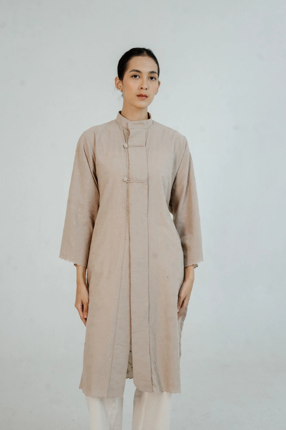 Woman wearing a beige long tunic by Damakara against a white background