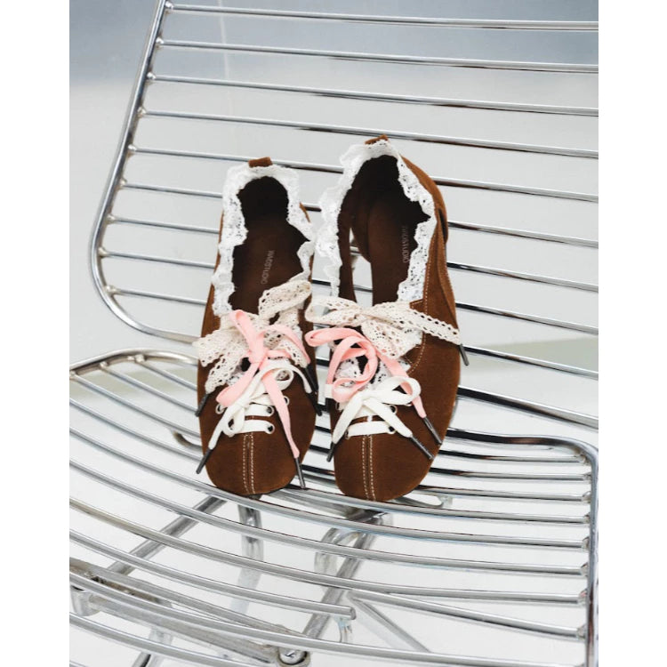 Brown flatshoes by Wad Studio with white laces and pink accents on a metal chair.
