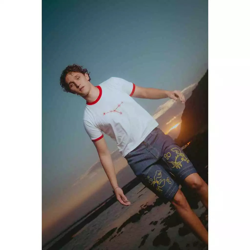 Person wearing a white t-shirt with red trim and dark jorts pants against a scenic background