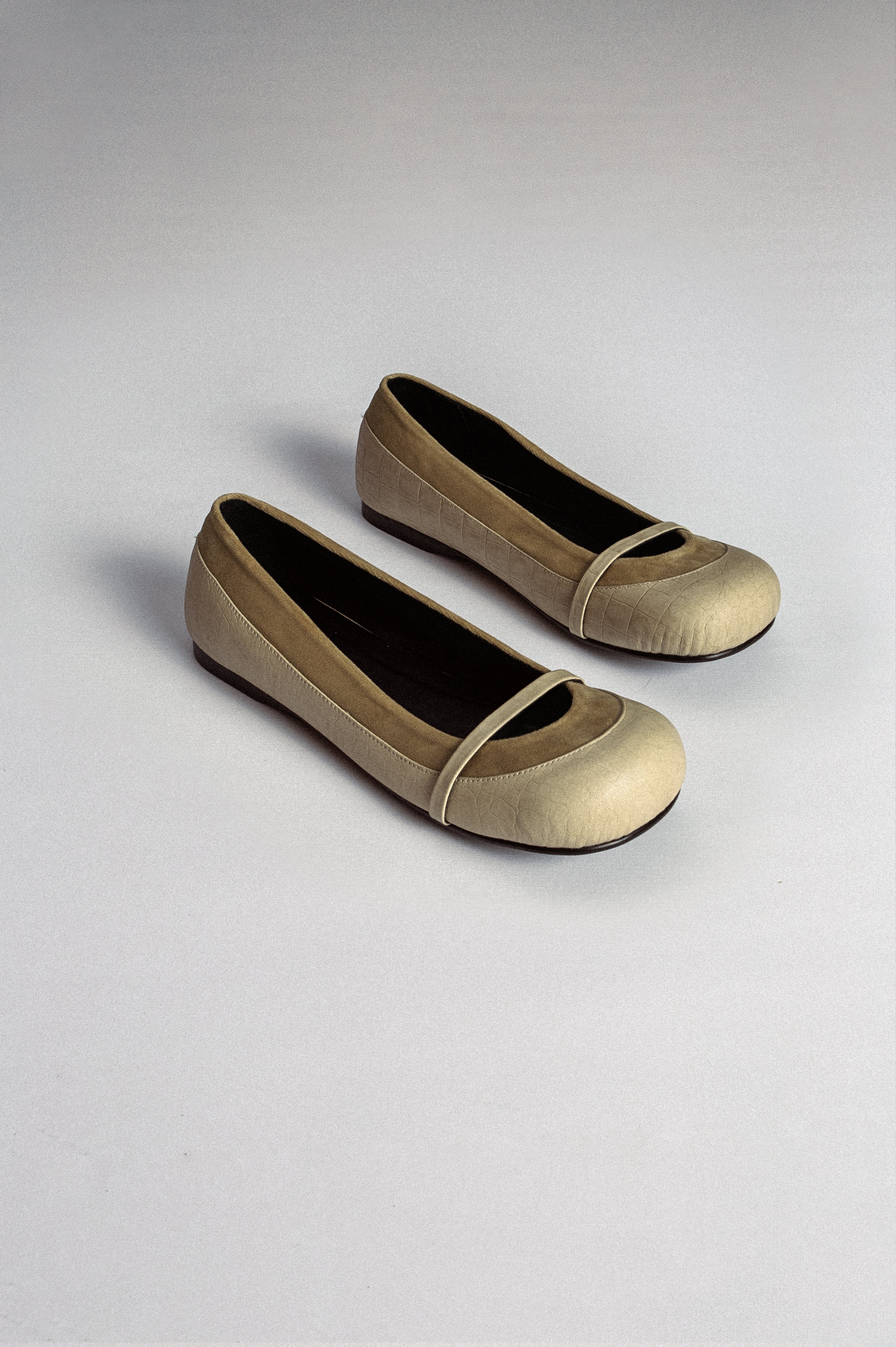 A pair of beige flat shoes with a crocodile pattern from MTW on a plain background.