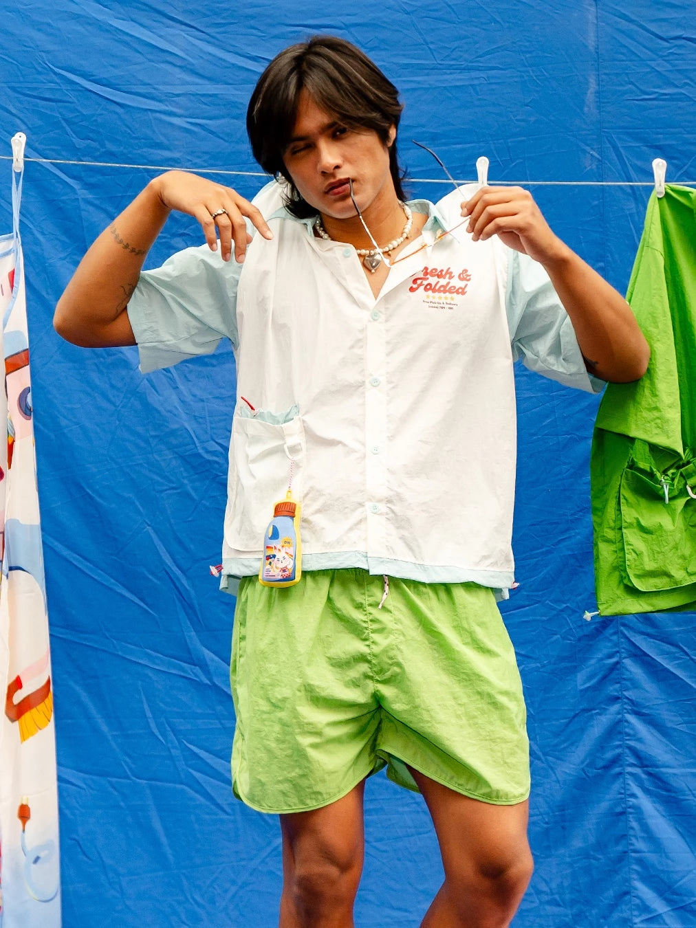Person wearing a white workshirt by Oh.Irv with red text and green shorts against a blue background