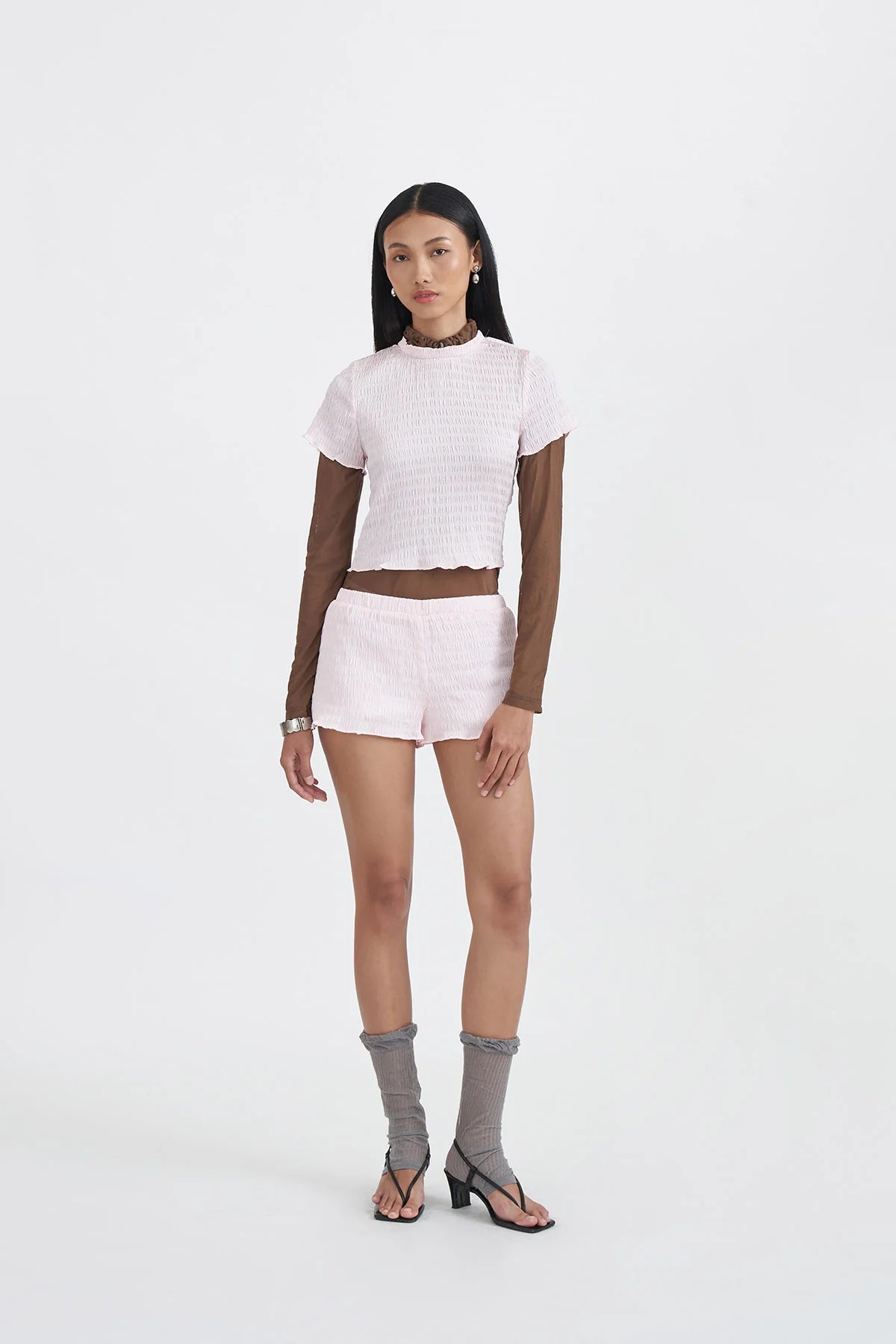 Woman wearing a light pink top by Callie Cotton, pink shorts, and gray socks on a white background