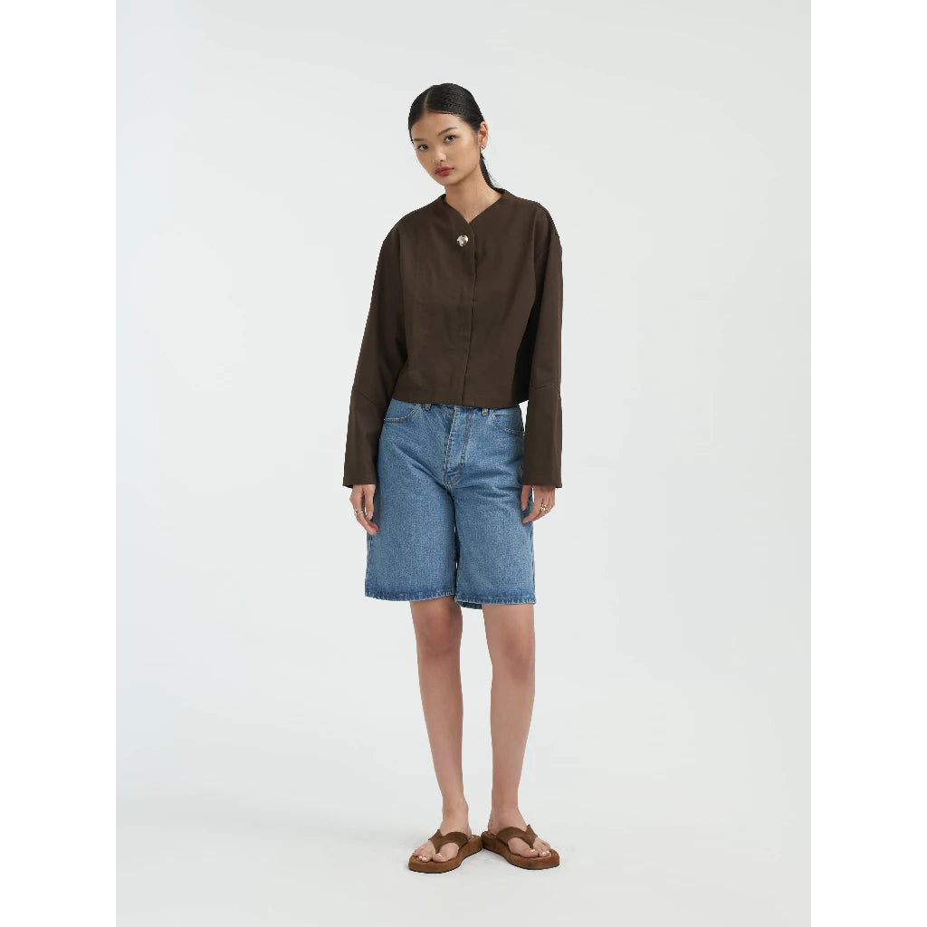 Woman wearing a brown jacket by Achete de Nous and blue denim shorts on a white background