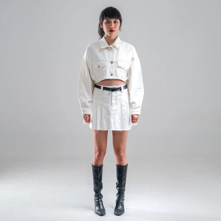 A model wearing a white denim skirt with a mini length, paired with a white top and black boots.
