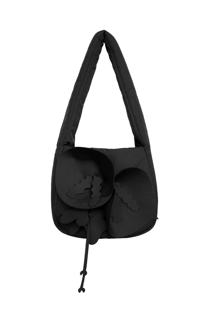 A black shoulder bag by Hunting Fields with a unique sculptural flower design on the front and a long strap, shown against a plain white background.