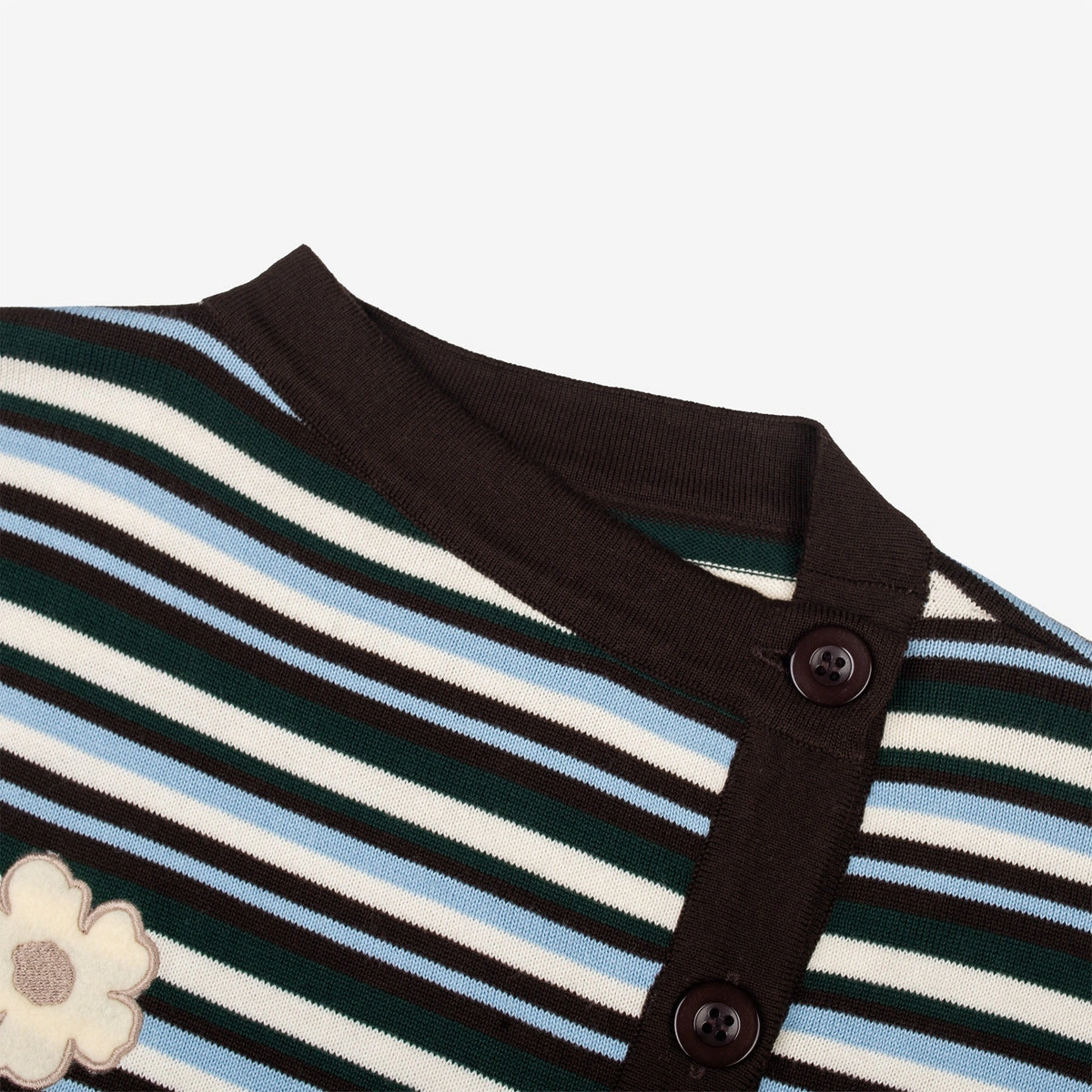 Close-up of a striped knit cardigan by Tome Ame with a dark brown ribbed collar and button placket, featuring horizontal stripes in dark green, black, cream, and light blue, with a cream flower applique on the left chest.