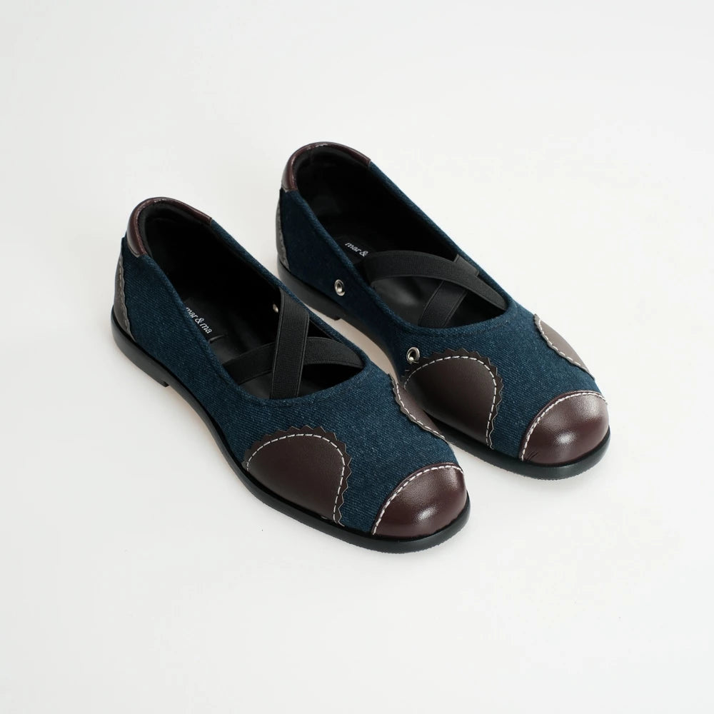 Pair of dark blue flat shoes with brown accents on a white background