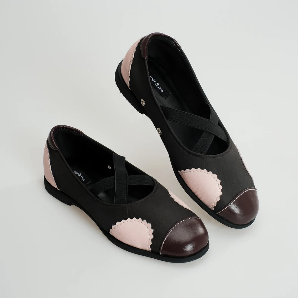 Black flat shoes with pink scalloped accents on a light gray background