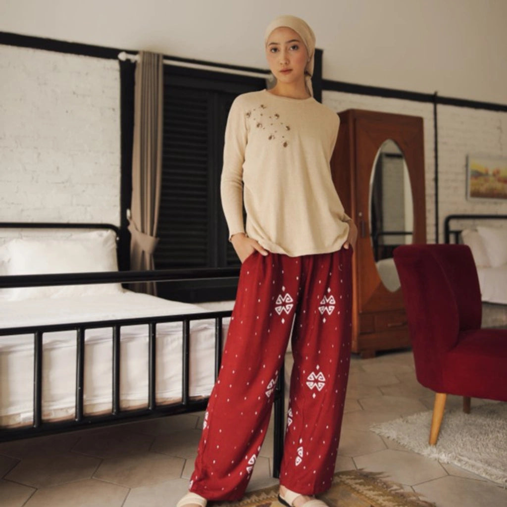 Person wearing a cream beads sweater from Damakara and red patterned pants in a room with furniture.