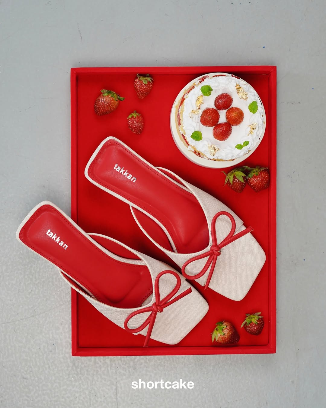 Red and white shoes with by Takkan, with strawberries and a dessert in a box on a gray background.