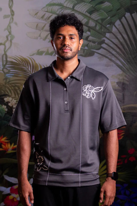 Man wearing a dark polo shirt with white embroidery by Nona against a tropical-themed background