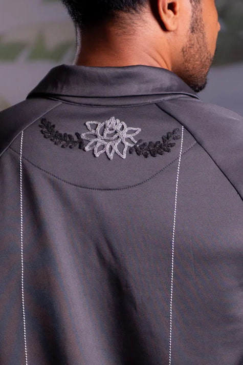 Gray polo shirt by Nona with floral embroidery on the back, worn by a person.