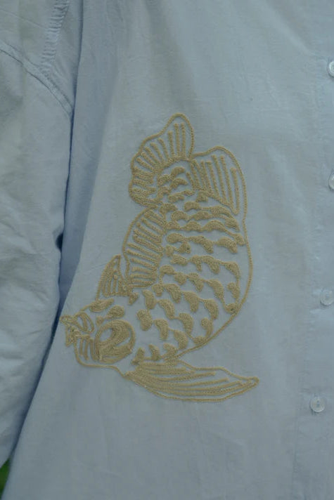 Light blue shirt with a gold embroidered fish design by Nona on a white background