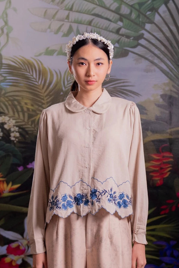 Woman wearing a beige shirt with floral embroidery by Nona against a tropical background