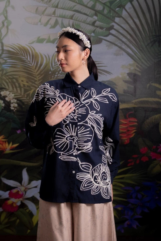 Woman wearing a dark blue floral-patterned shirt by Nona against a tropical background