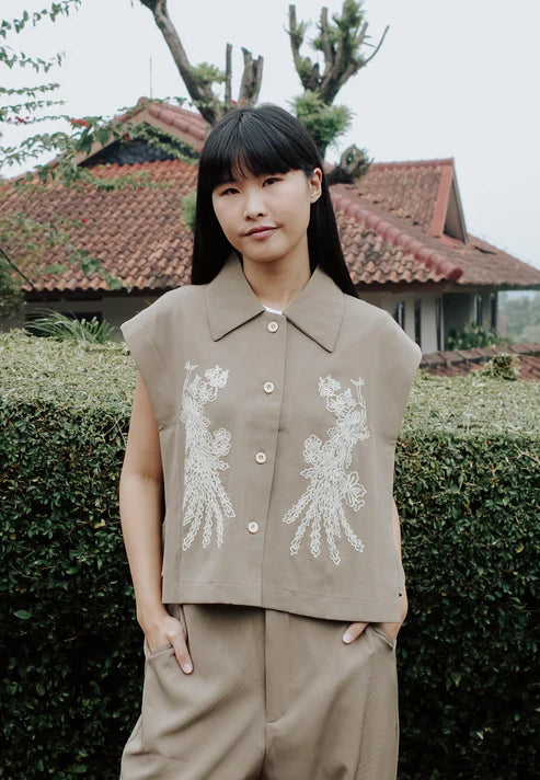 Person wearing Nonaetal Hibiscus Vest, a beige vest with floral embroidery, in an outdoor setting.