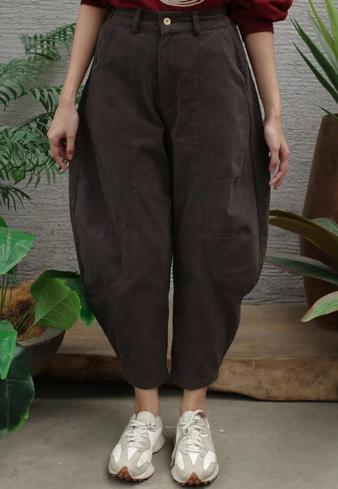 Person wearing brown high-waisted barrel pants standing indoors with plants in the background