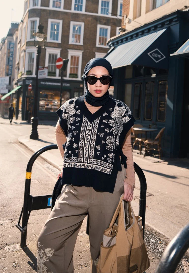 Woman wearing Nonaetal Serenity Orchid Knit Vest, a black and white patterned knitted vest, with beige pants on a city street.