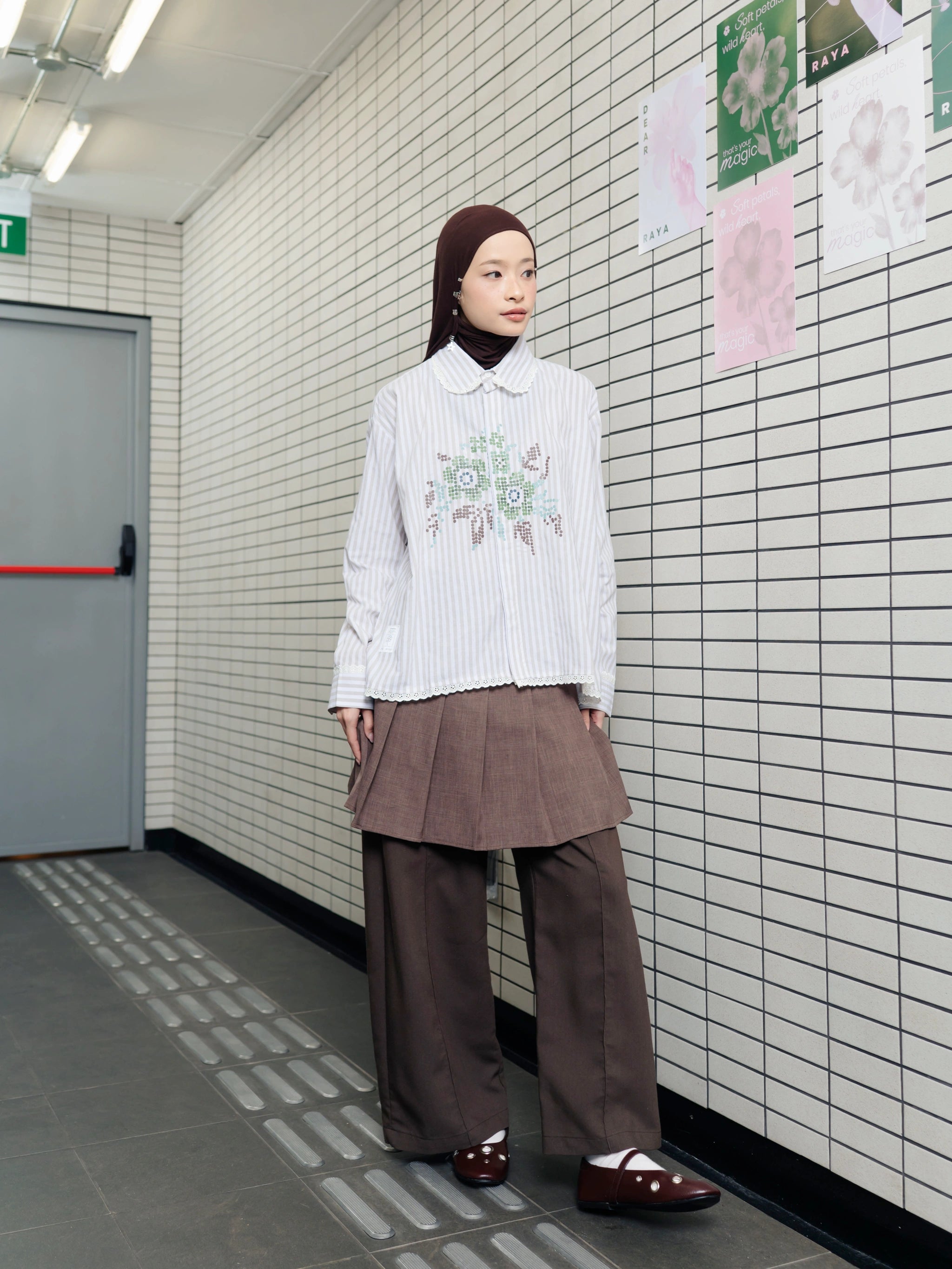 Person wearing a white long-sleeved shirt by Tome Ame with floral embroidery and brown pants in a subway setting.