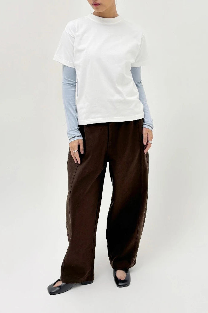 Person wearing a white top, light blue long-sleeve shirt, and brown wide-leg barrel pants on a white background