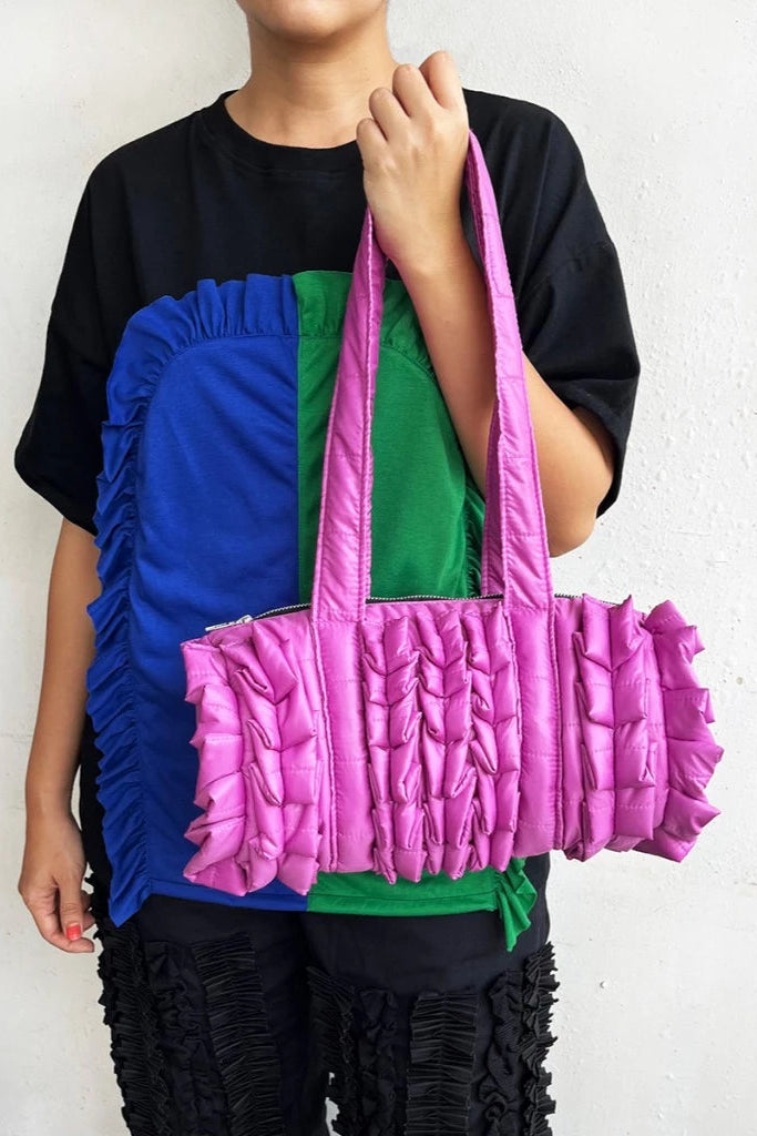 Person holding a colorful quilted duffle bag by Mannequin Plastic against a plain background