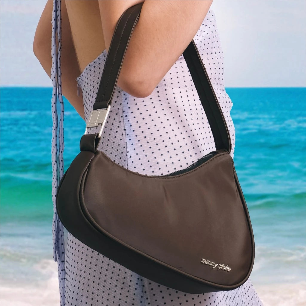 A sleek brown women’s shoulder bag with a modern crescent silhouette, featuring a smooth finish and a subtle metal “sunny pixie” logo on the front. The slim strap adds a minimalist touch, making it perfect for everyday wear or casual outings.
Tas wanita cokelat dengan siluet crescent yang modern, dilengkapi permukaan yang sleek dan logo metal “sunny pixie” di bagian depan. Tali bahu yang ramping memberi sentuhan minimalis, ideal untuk dipakai sehari-hari maupun saat hangout santai.