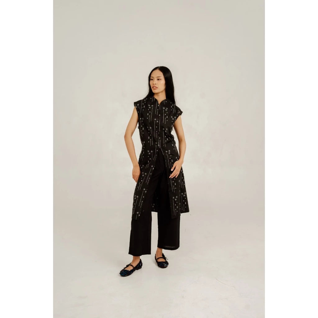 Woman wearing a black patterned kebaya by Damakara on a white background
Seorang wanita mengenakan kebaya lengan pendek berwarna hitam bermotif dari Damakara dengan latar belakang putih