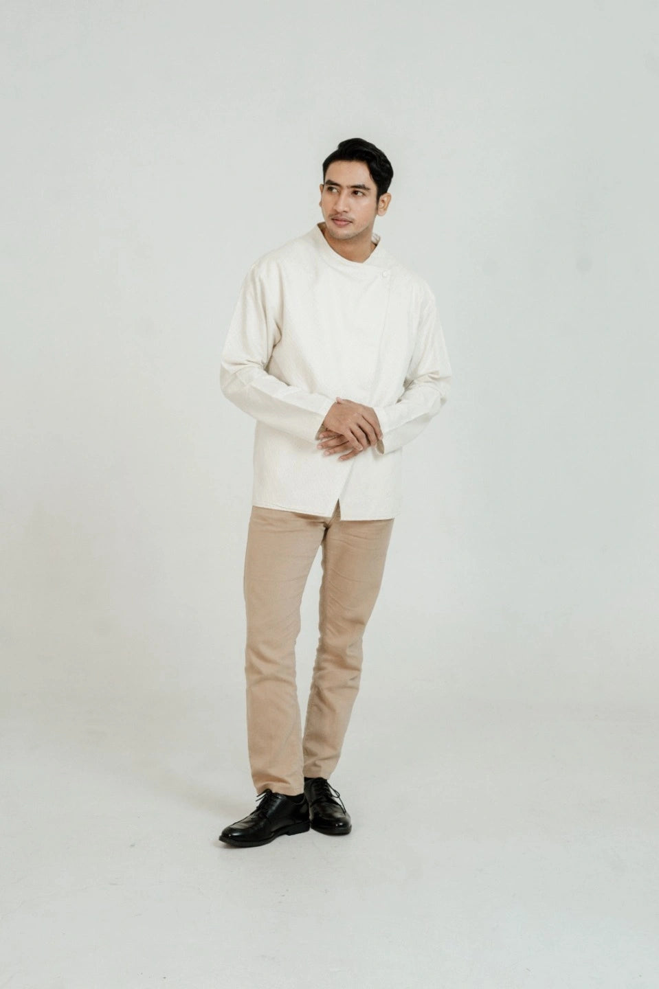 Man wearing a white beskap by Damakara and beige pants on a white background