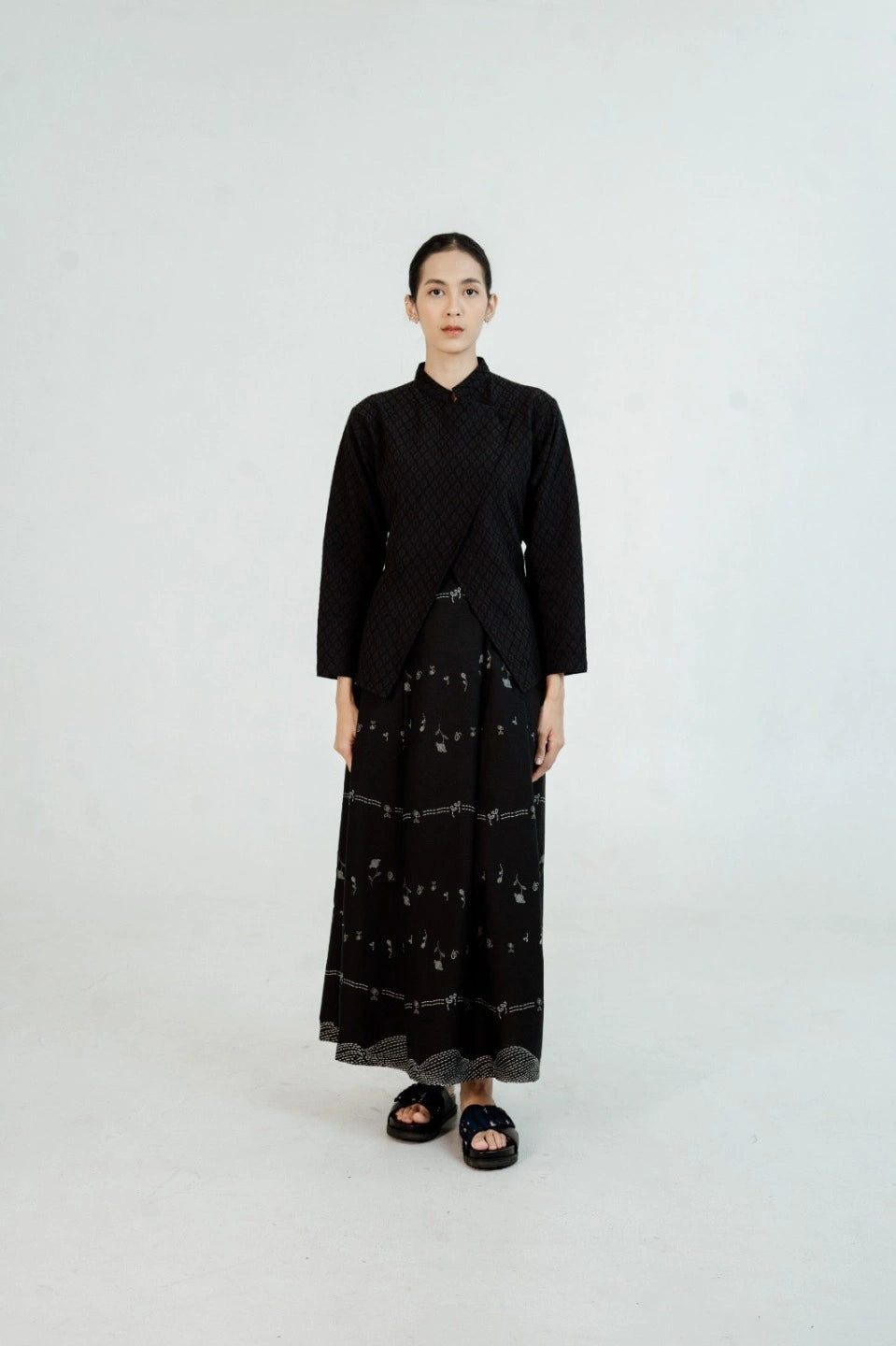 Person wearing a black suit by Damakara with a patterned skirt on a white background