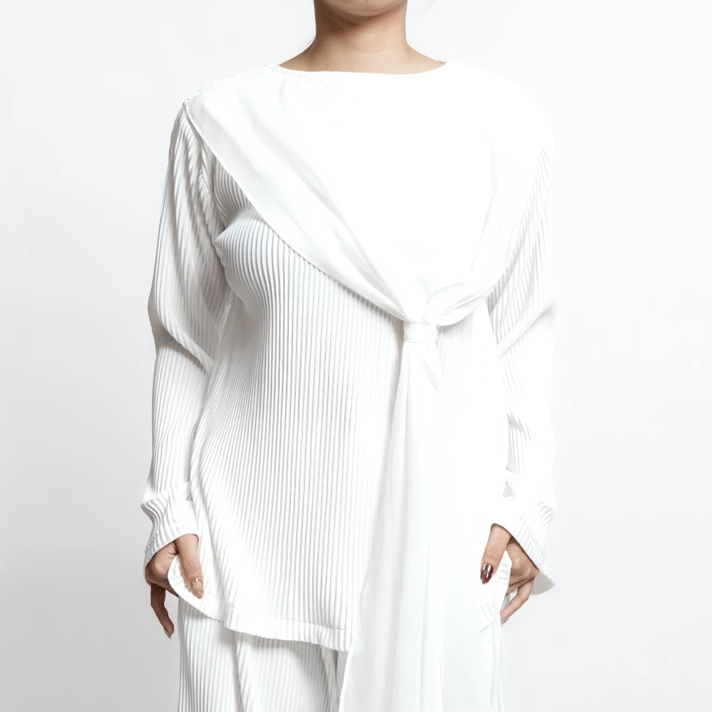Person wearing a white pleated top by Isoos Stuidos with a flowing design on a plain background