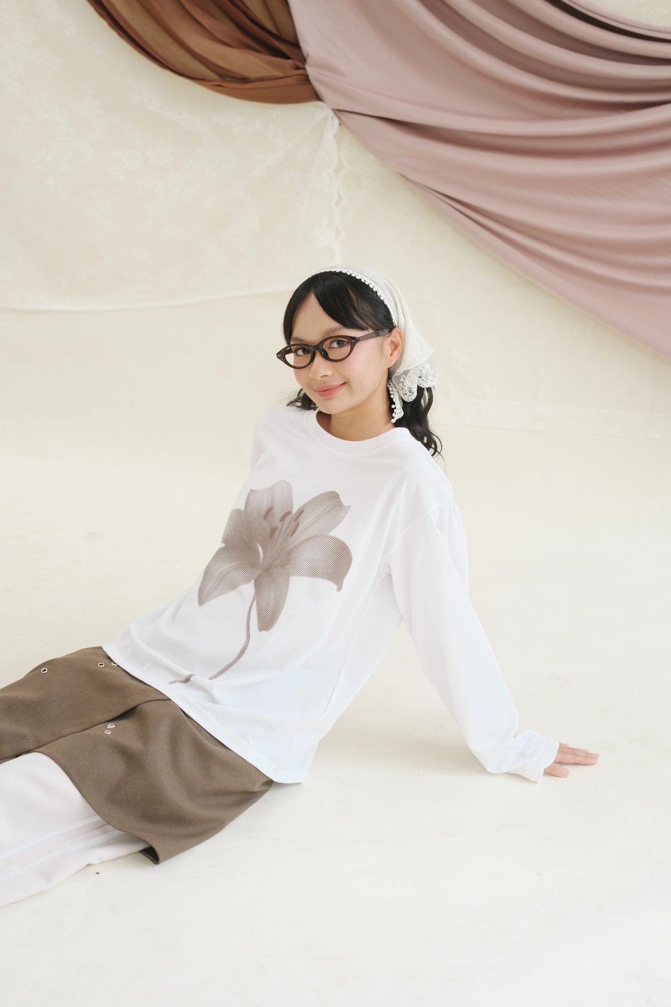 Person wearing a white long-sleeve t-shirt by Tome Ame with a gray flower design and brown pants on a light background