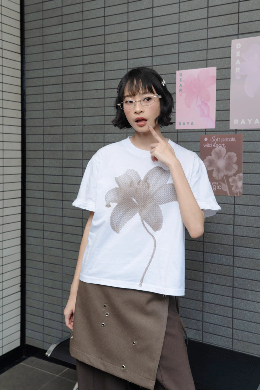 Person wearing a white t-shirt by Tome Ame with a flower design in an indoor setting.