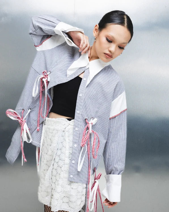 Person wearing a gray striped shirt with decorative ribbons by Wad Studio against a neutral background