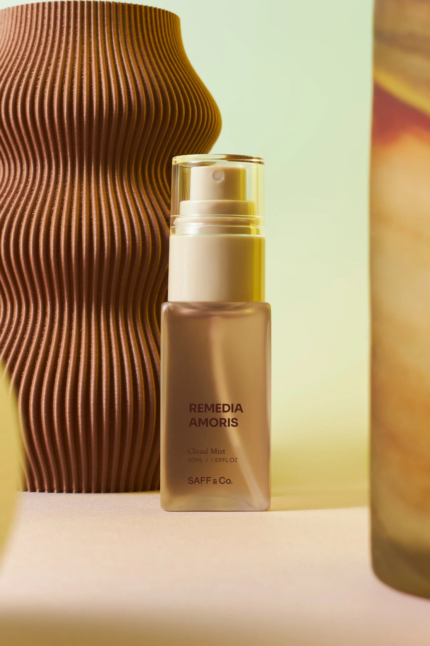 Body mist bottle labeled 'Remedia Amoris' by Saff & Co with decorative vases in the background