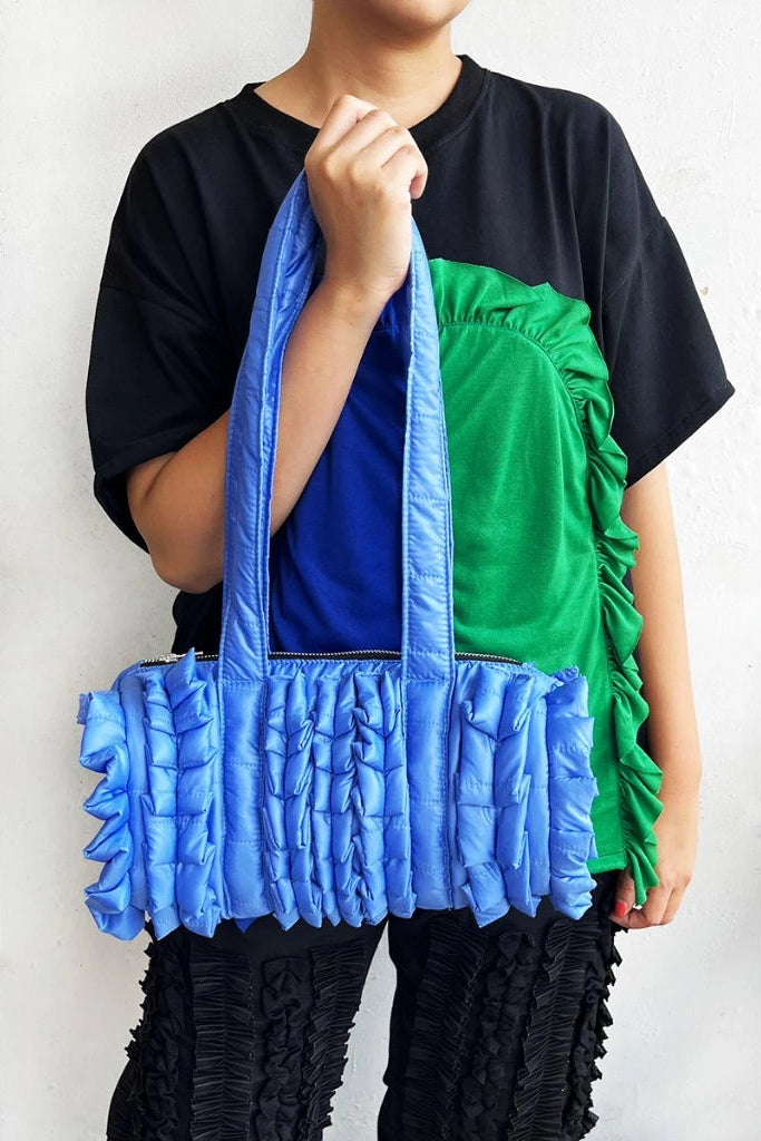 Person holding a blue ruffled duffle bag by Mannequin Plastic against a white background