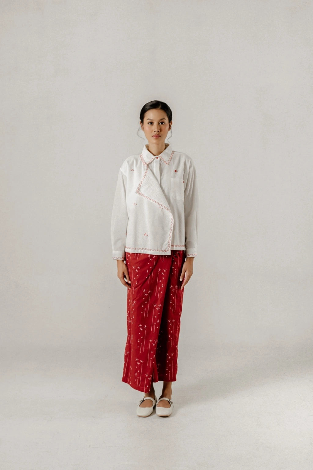 Person wearing a white top by Damakara and red patterned skirt on a plain background