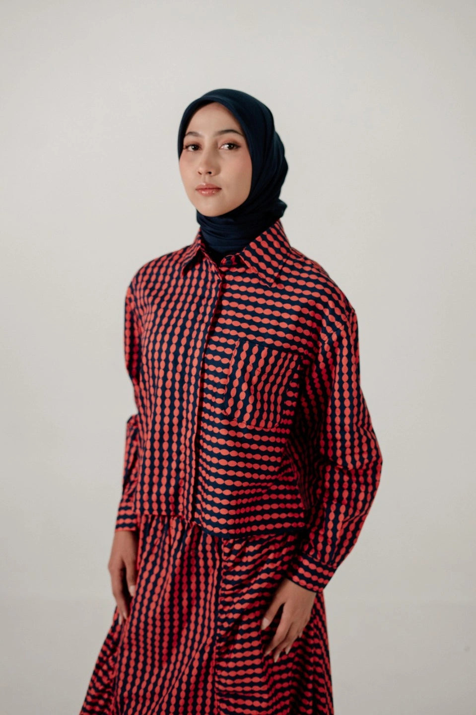 Person wearing a red and navy checkered longsleeve shirt by Damakara with a headscarf against a plain background
