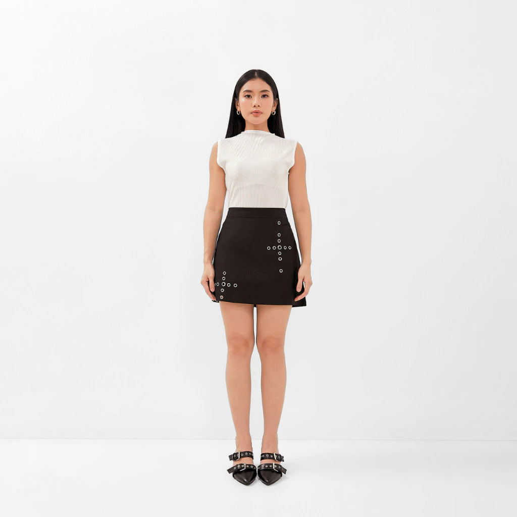 Woman wearing a white top and black mini skirt with button details on a white background