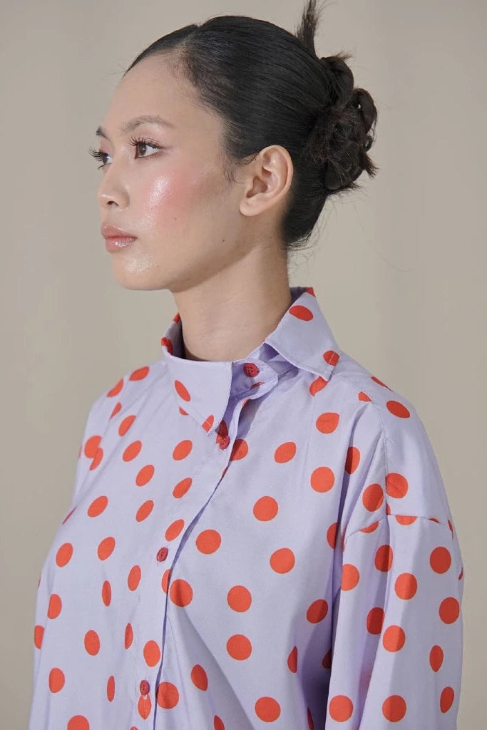 Woman wearing a light purple shirt with red polka dots by Tuff Puff against a plain background