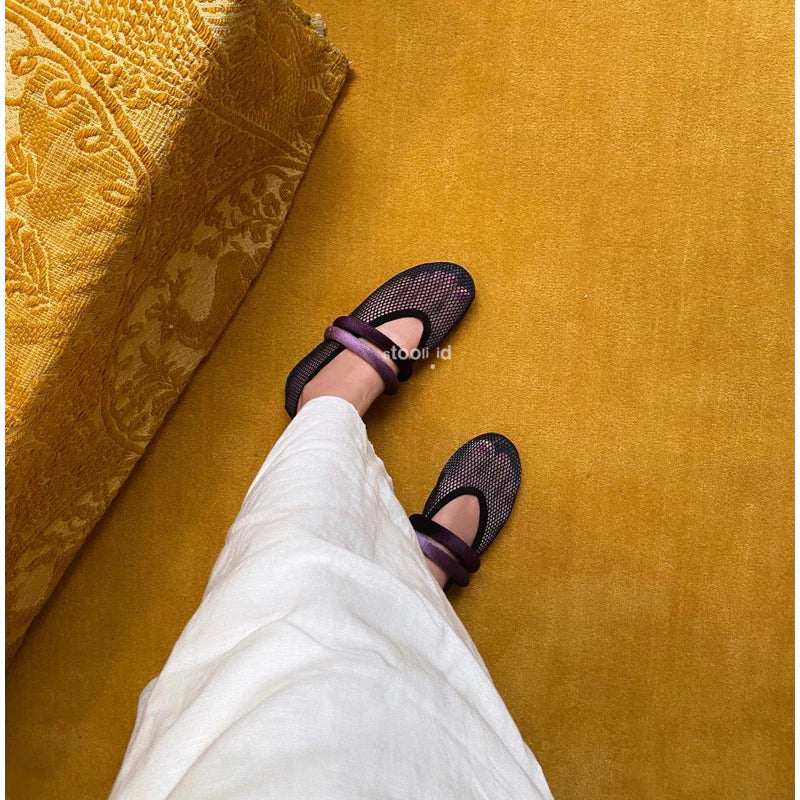Women’s black mesh flatshoes with purple crisscross elastic straps on a yellow carpet background.