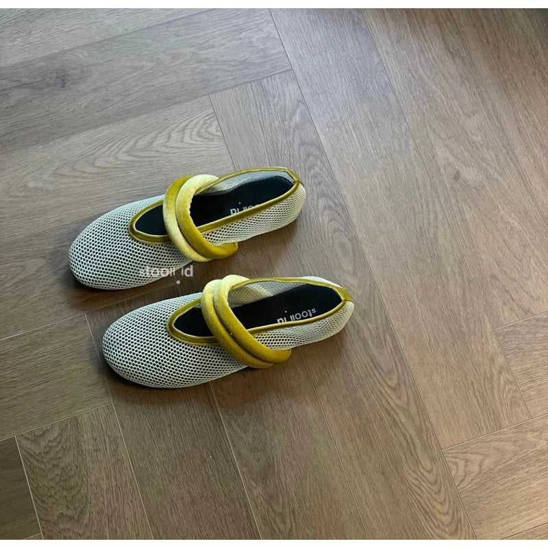 Women’s white mesh flatshoes with yellow crisscross elastic straps on a wooden background.