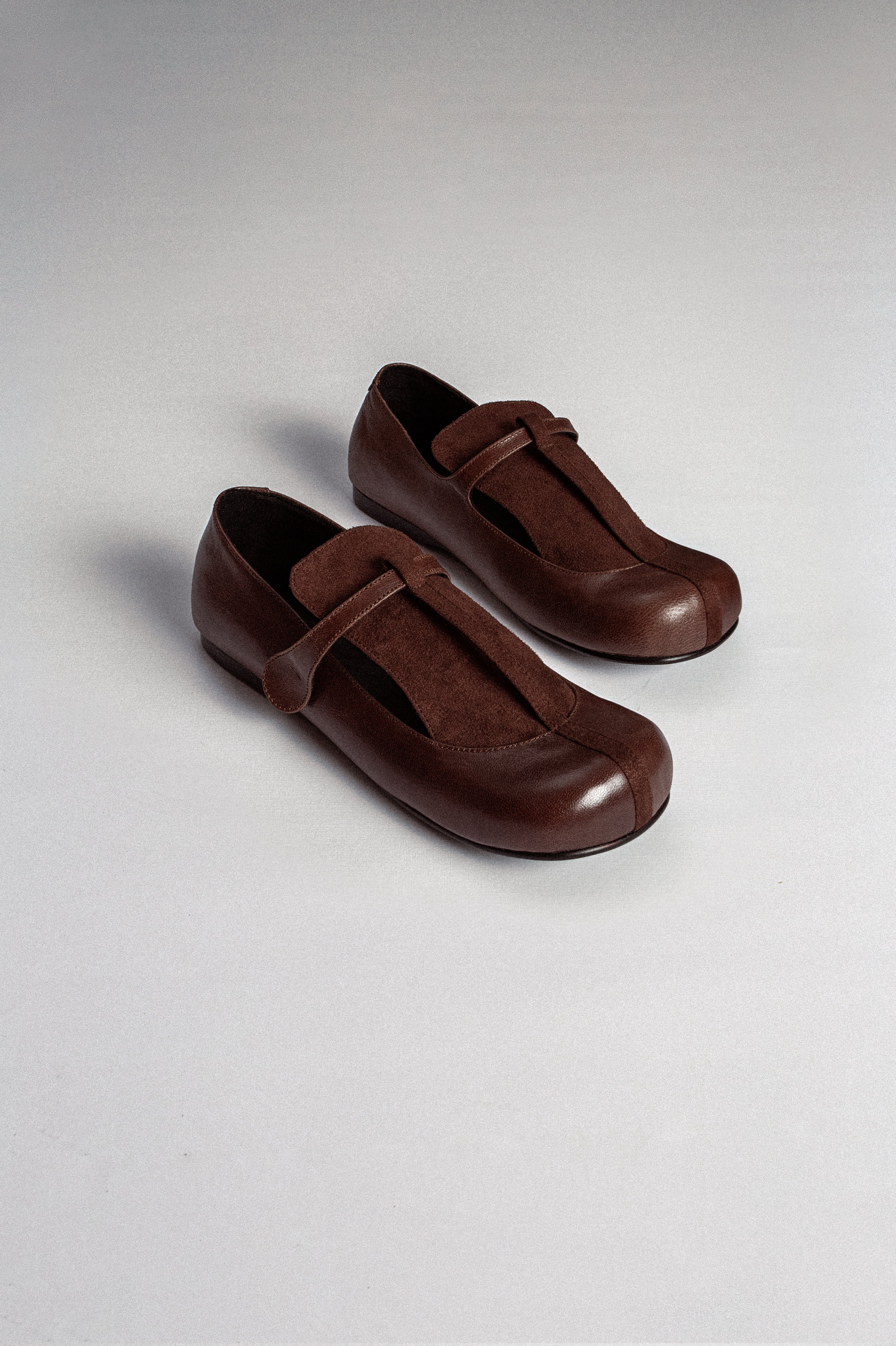 A pair of brown leather flat shoes with a T-bar closure system from MTW, displayed against a white background.
