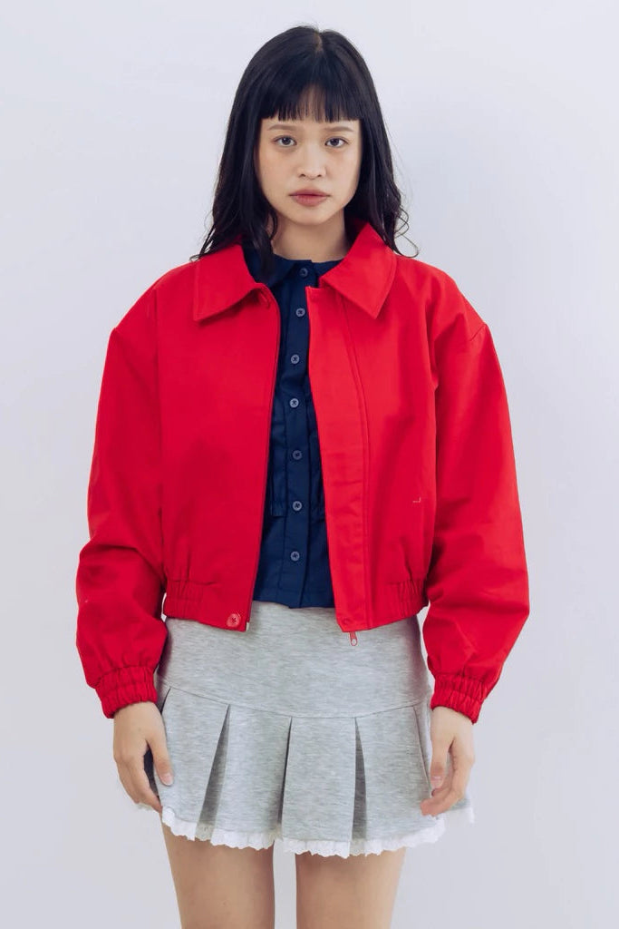 Person wearing a red jacket by notyourcompany and gray pleated skirt on a white background