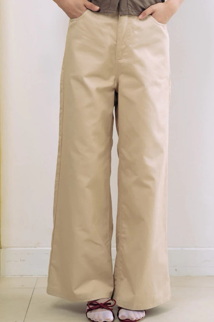 Person wearing beige wide-leg pants by notyourcompany against a white wall.