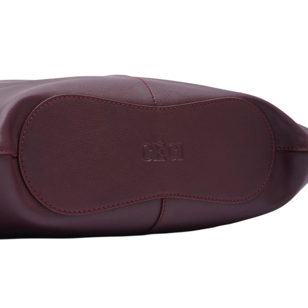 Close-up of a maroon leather handbag with 'Ceci' branding on a white background
Close-up tas tangan wanita berbahan kulit berwarna maroon dengan merek ‘Ceci’ pada latar belakang putih.