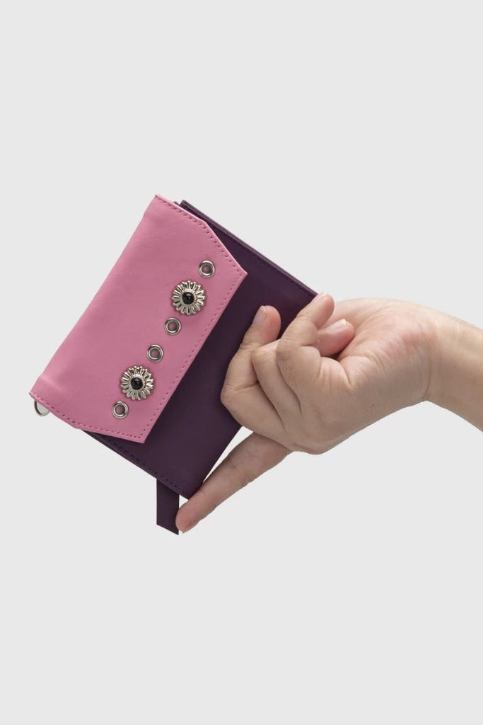 Hand holding a pink and purple wallet by Adorable Projects against a white background