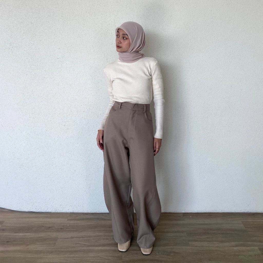 Woman wearing a white top and light brown barrel pants standing against a plain wall.
Seorang wanita yang mengenakan atasan putih dan celana barrel berwarna cokelat muda sedang berdiri di depan dinding polos.